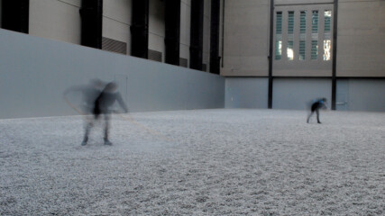 Photo of Ai Wei Wei's Sunflower Seeds, Tate Modern, London. Two members of staff are tending to the installation, one in the foreground and one in the back.