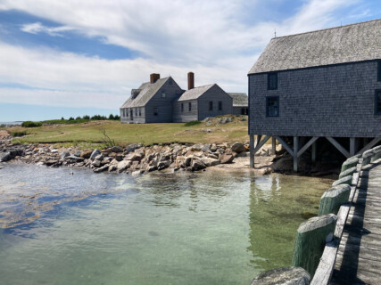 Photo taken from a jetty looking back at a sunny island scene with some Maine style houses