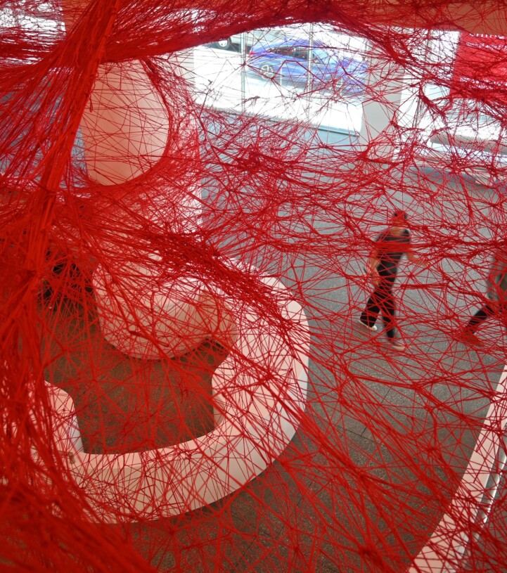 Photo from the galleries of a red mesh artwork. People can be seen moving through the gallery, beyond the artwork.