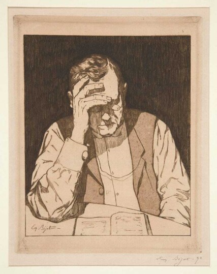 man wearing reading glasses sitting at a table reading a book