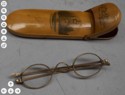 screenshot of an image viewer displaying a photo of 19th century brass spectacles with brown wooden case. image viewer controls arranged along the left side top to bottom contain zoom buttons, a reset button, and options, download, and lock button. in the bottom left corner there are 4 arrow buttons to move around the image.