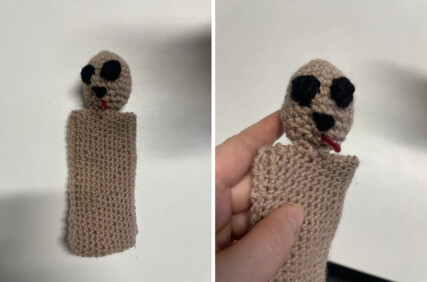 A rectangle of pink knitted material with a sphere at the top. The sphere has two eyes, a nose and a tongue.
